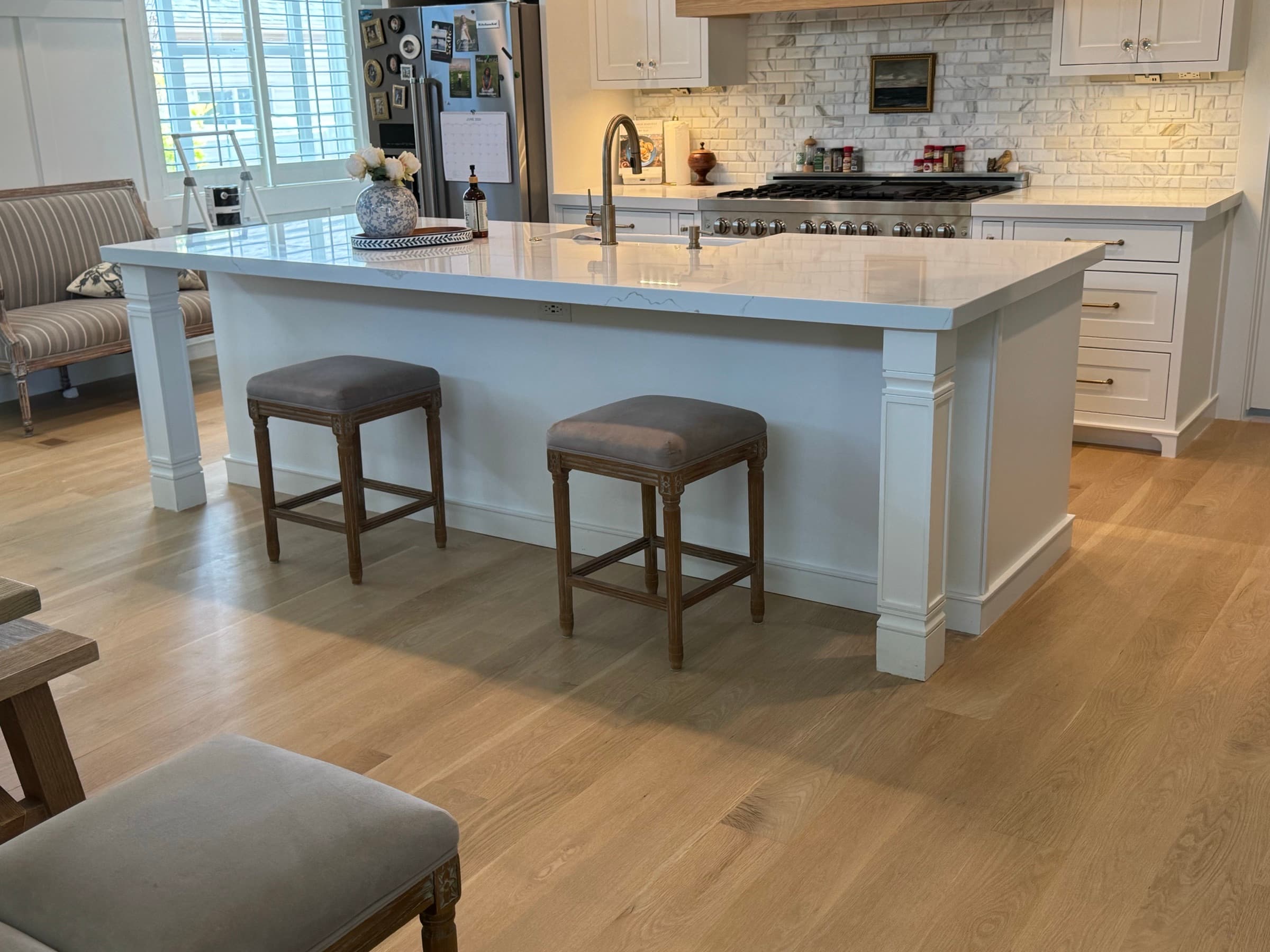 Large white quartz island with upholstered stools and oak floors