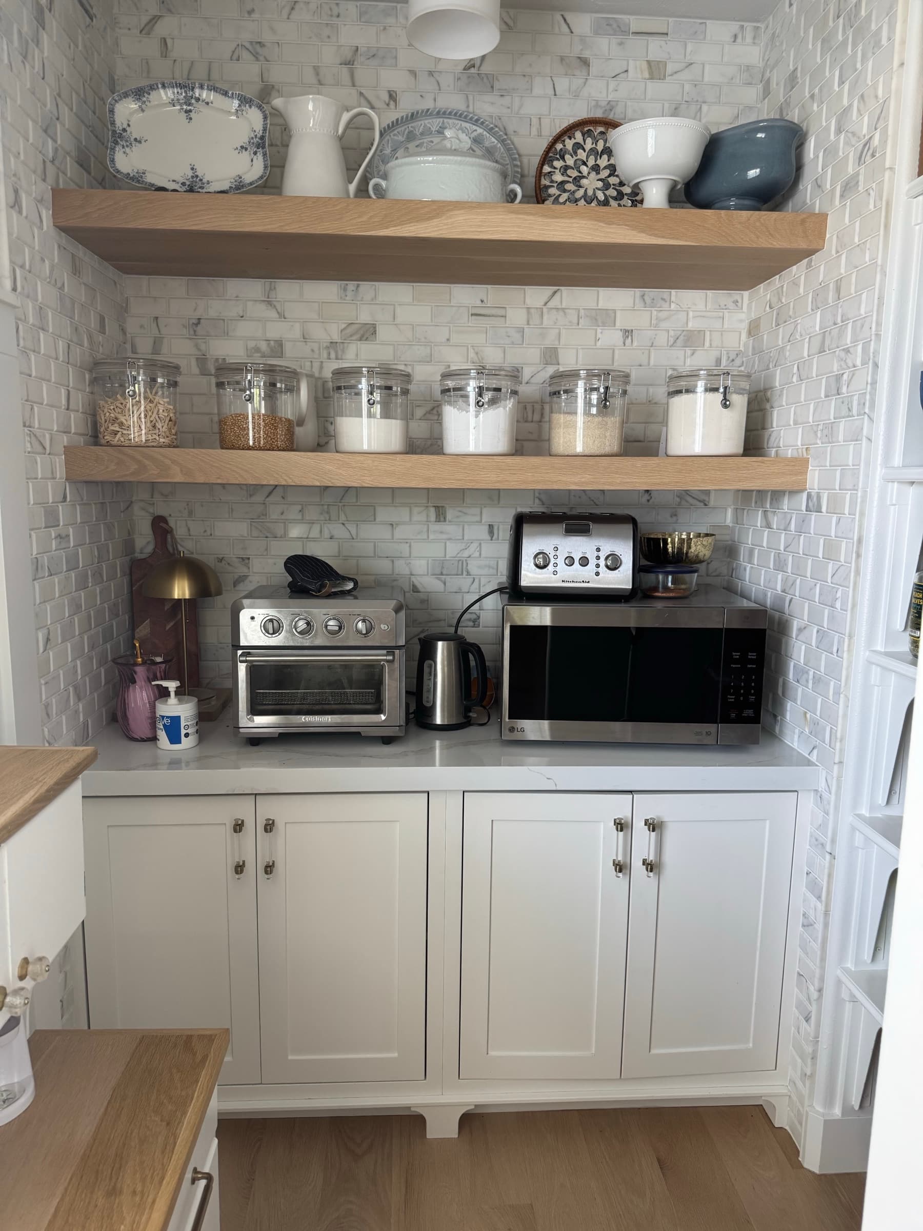White pantry nook with floating oak shelves and marble tile